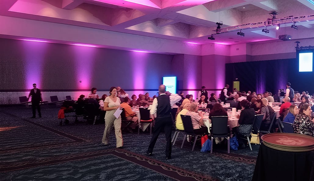 Large convention center conference hall transformed with professional architectural uplighting, brand-matched colors, and full-room production coverage for a major corporate event